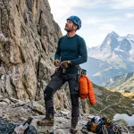Arrampicatore con abbigliamento tecnico a strati, pantaloni rinforzati e imbrago alla base della falesia
