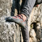 Dettaglio della scarpetta da arrampicata posizionata di punta su una tacca di calcare