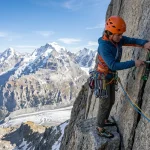Alpinista che piazza un friend in fessura granitica su via multipitch con mezze corde e moschettoni