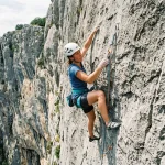 Climber che pratica free climbing assicurato su una parete di roccia calcarea