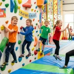 Bambini e istruttrice che svolgono giochi di arrampicata su parete boulder colorata con materassi morbidi