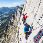 Arrampicatori su parete verticale con mezze corde rosse e blu in sosta durante una salita multipitch