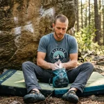 Arrampicatore seduto su crash pad con maglietta grafica tecnica da boulder e sacchetto magnesite